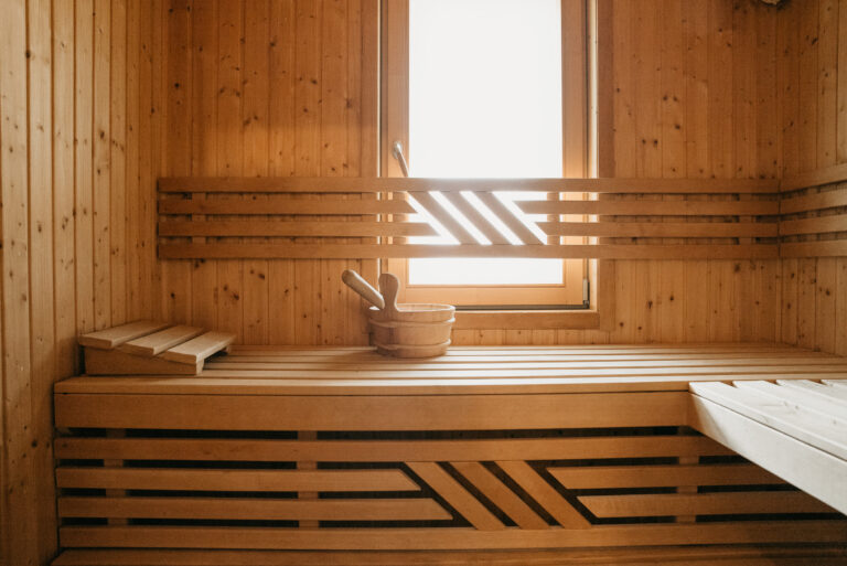 Querformatige Innenaufnahme der Sauna im Ferienhaus Traumfänger mit Holzbank, Aufguss-Eimer und schmalem Fenster mit Lichteinfall.